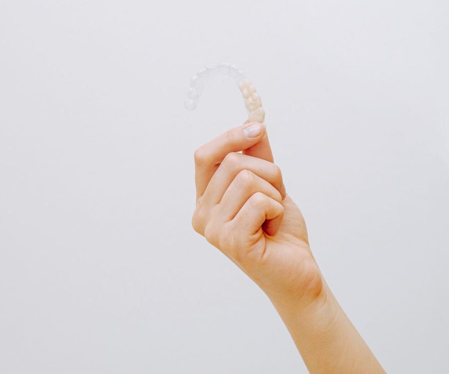 A hand holding a single clear aligner tray